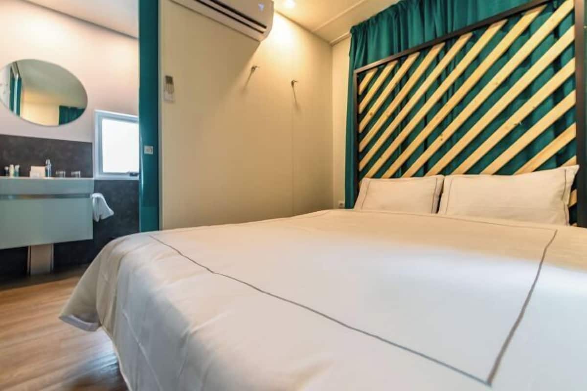 A hotel room with a bed, a bathroom with a mirror, and a window.