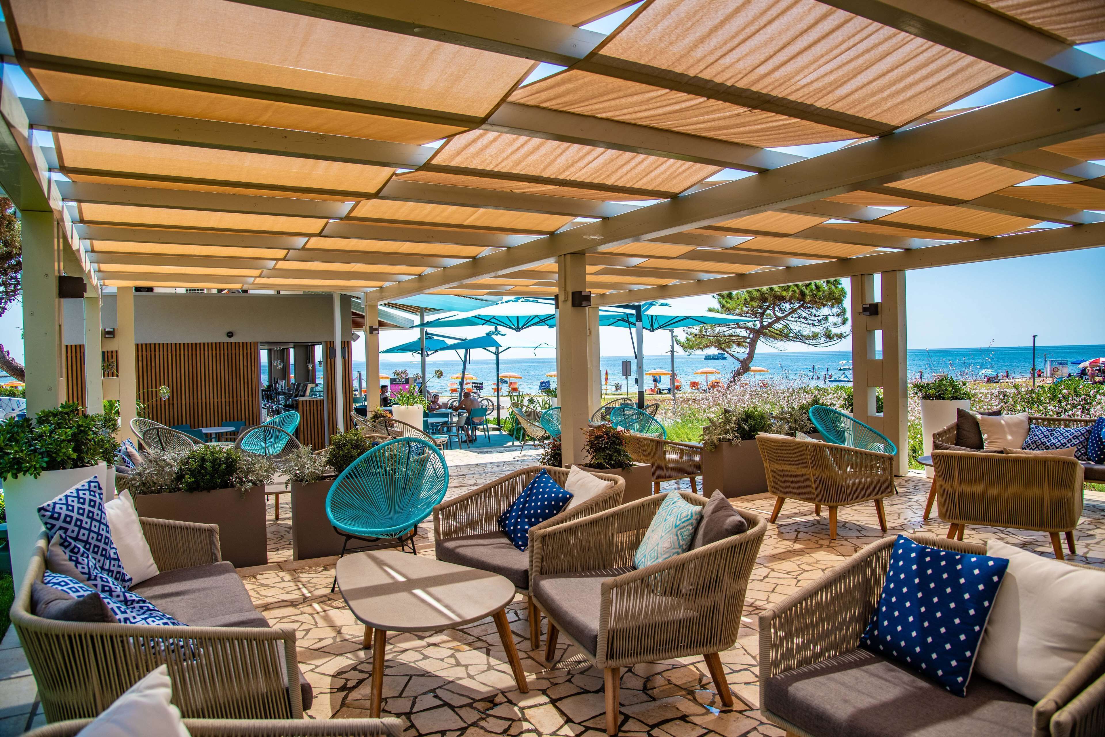 An outdoor seating area with wicker furniture and umbrellas, overlooking a beach.