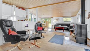 Uma sala de estar ampla com um sofá de couro preto, uma mesa de jantar e uma lareira a lenha de madeira preta.