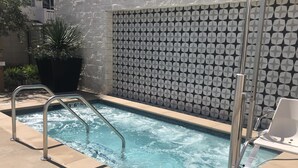 Ein Schwimmbecken mit einer Metallleiter, einer Kachelwand mit geometrischem Muster und einer Liege.