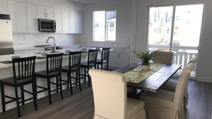 Eine moderne Küche mit weißen Schränken, einer Mikrowelle und einem Spülbecken. Es gibt einen Essbereich mit Tisch, Stühlen und einem Blumentopf.