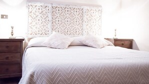 Un lit bien fait, avec une couvre-lit à motifs, une tête de lit décorative et des tables de chevet dotées de lampes.