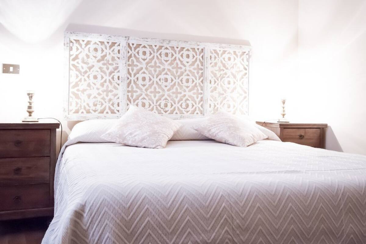 A neatly made bed with a patterned bedspread, a decorative headboard, and bedside tables with lamps.