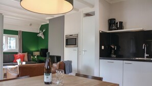 A modern kitchen with a built-in oven and microwave, a dining area with a wooden table, and a living room with a sofa and a green accent wall.