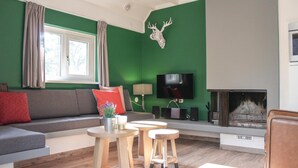 A modern living room with a green accent wall, a fireplace, a sofa with cushions, a television, and a mounted deer head.