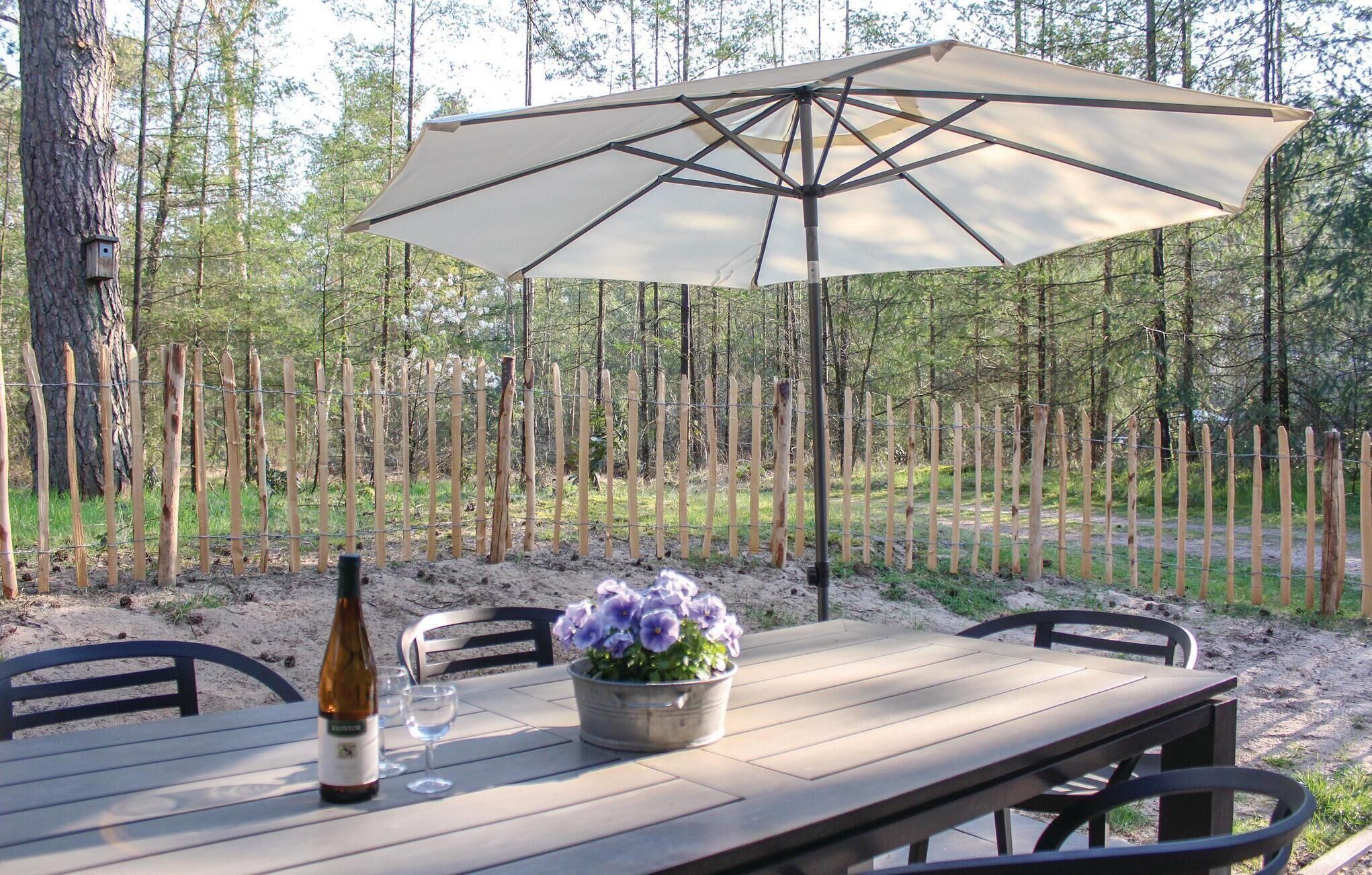 Een terras met een tafel, stoelen, een parasol, een fles wijn en een bloempot.