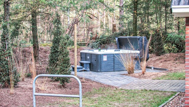 A hot tub in a wooded area with a brick pathway leading to it.
