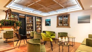 Cómoda sala de estar con sillones tapizados de verde, techo de madera y una estantería llena de botellas.