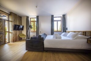 A bedroom with a large bed, a flat-screen TV mounted on the wall, a wooden floor, and a window with curtains. - La Garenne (Saverne)