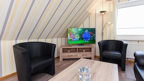 Ett mysigt rum med en tv, två svarta läderfåtöljer, ett träbord och randig tapet.