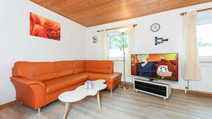 Ett vardagsrum med en hörnsoffa, en platt-TV, ett soffbord och en tavla på väggen.