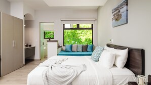 Un dormitorio moderno con una cama grande, vistas a zonas verdes por una ventana, un banco empotrado y una zona de cocina.