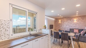 Een moderne keuken met een groot raam, een eethoek met een tafel en stoelen, en een zithoek met een bank.