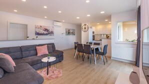 Een moderne woonkamer met een grijze bank, een ronde salontafel en een eethoek met een witte tafel en stoelen.