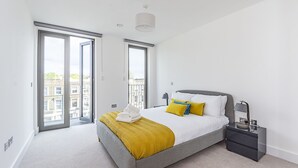 Un dormitorio moderno con una cama grande, una mesita de noche y vistas a la ciudad a través de una puerta corrediza.