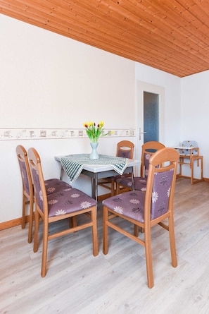 Uma sala de jantar com mesa, cadeiras e um vaso de flores.