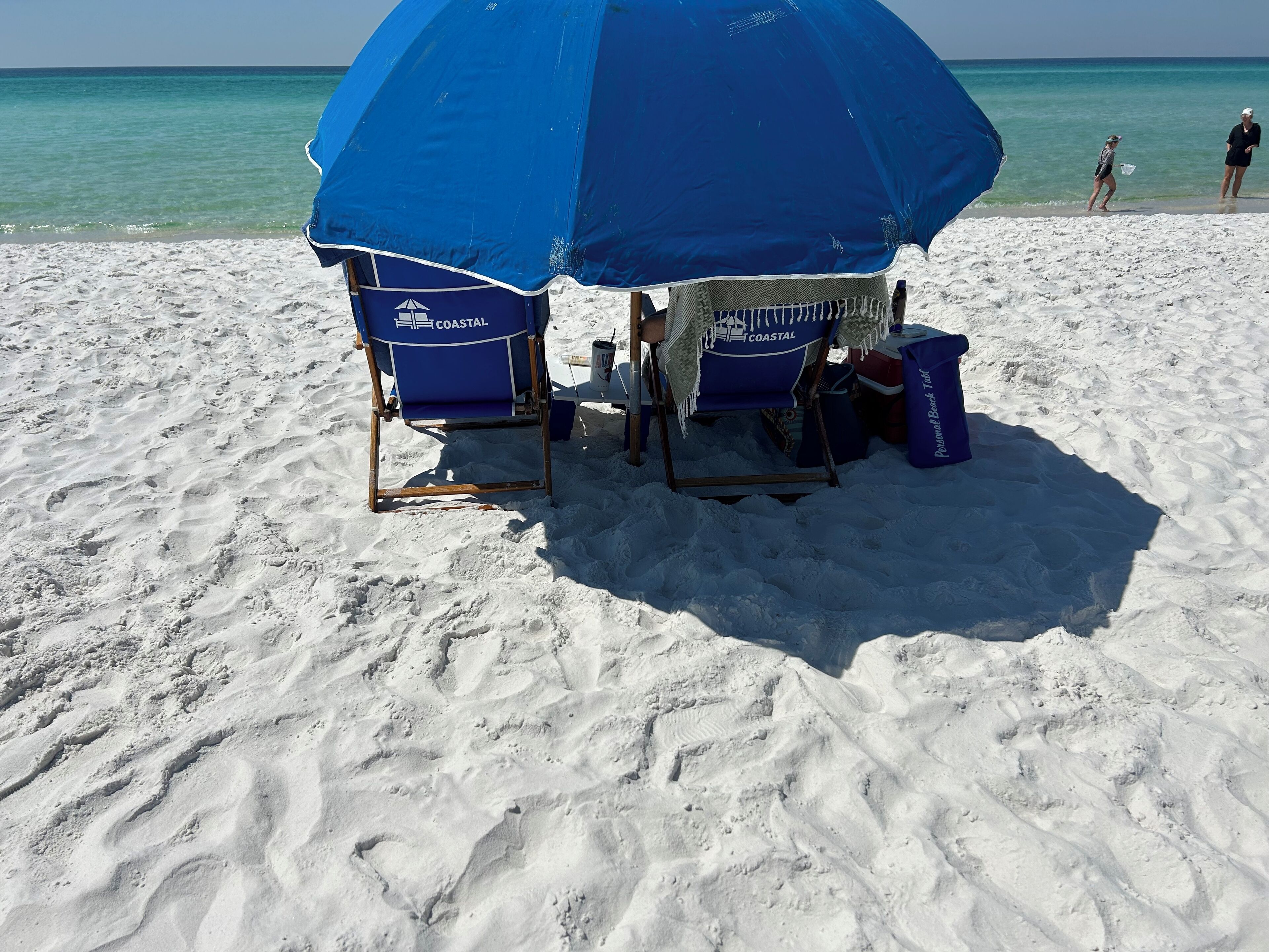 A beach umbrella providing shade over two chairs labeled 'COASTAL'.