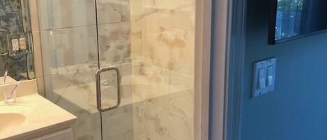 Une salle de bain avec une douche à parois de verre, un lavabo blanc et un sol carrelé.