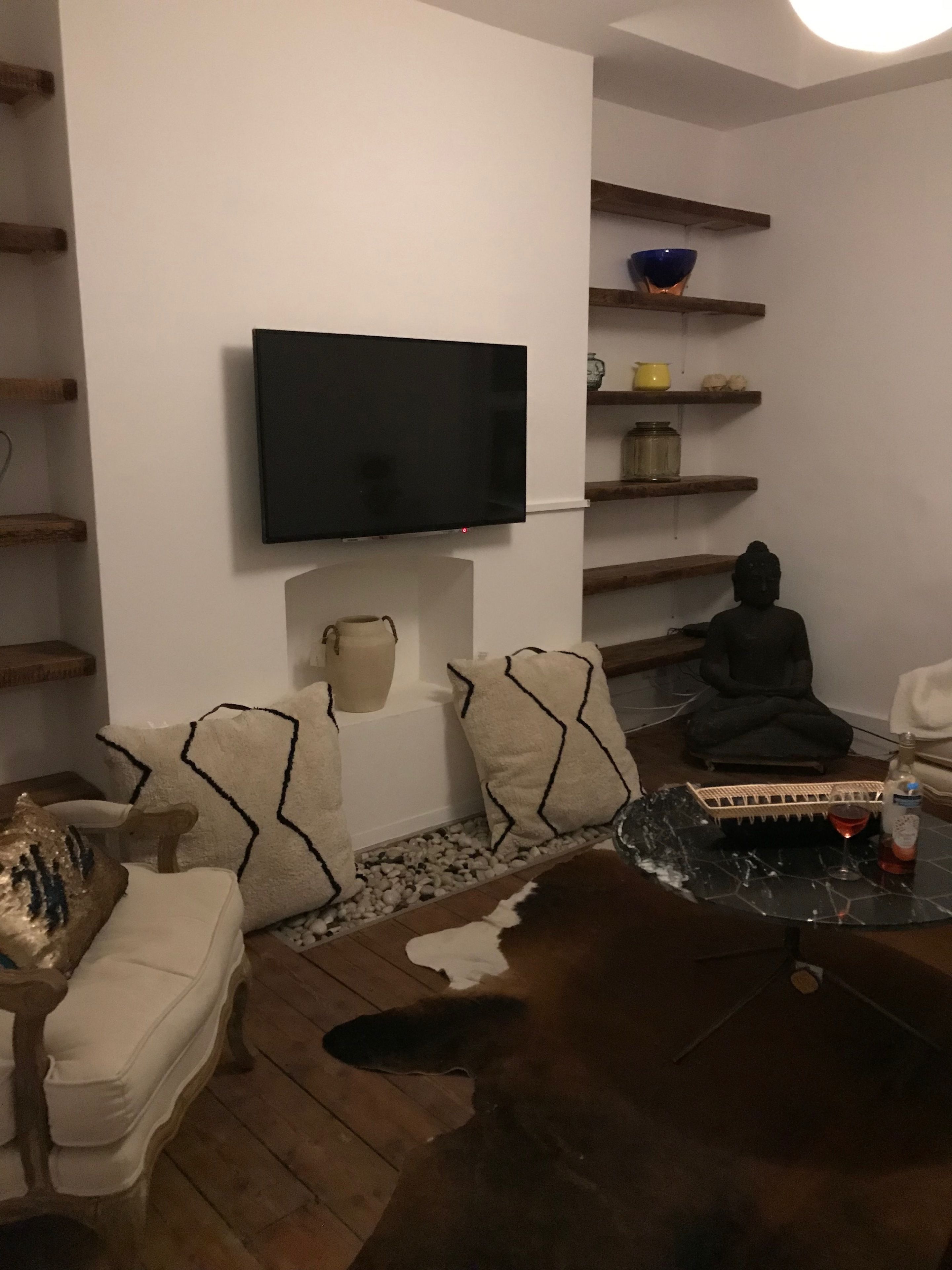 A living room with a flat-screen TV mounted on the wall, a meditation statue, and shelves with decorative items.