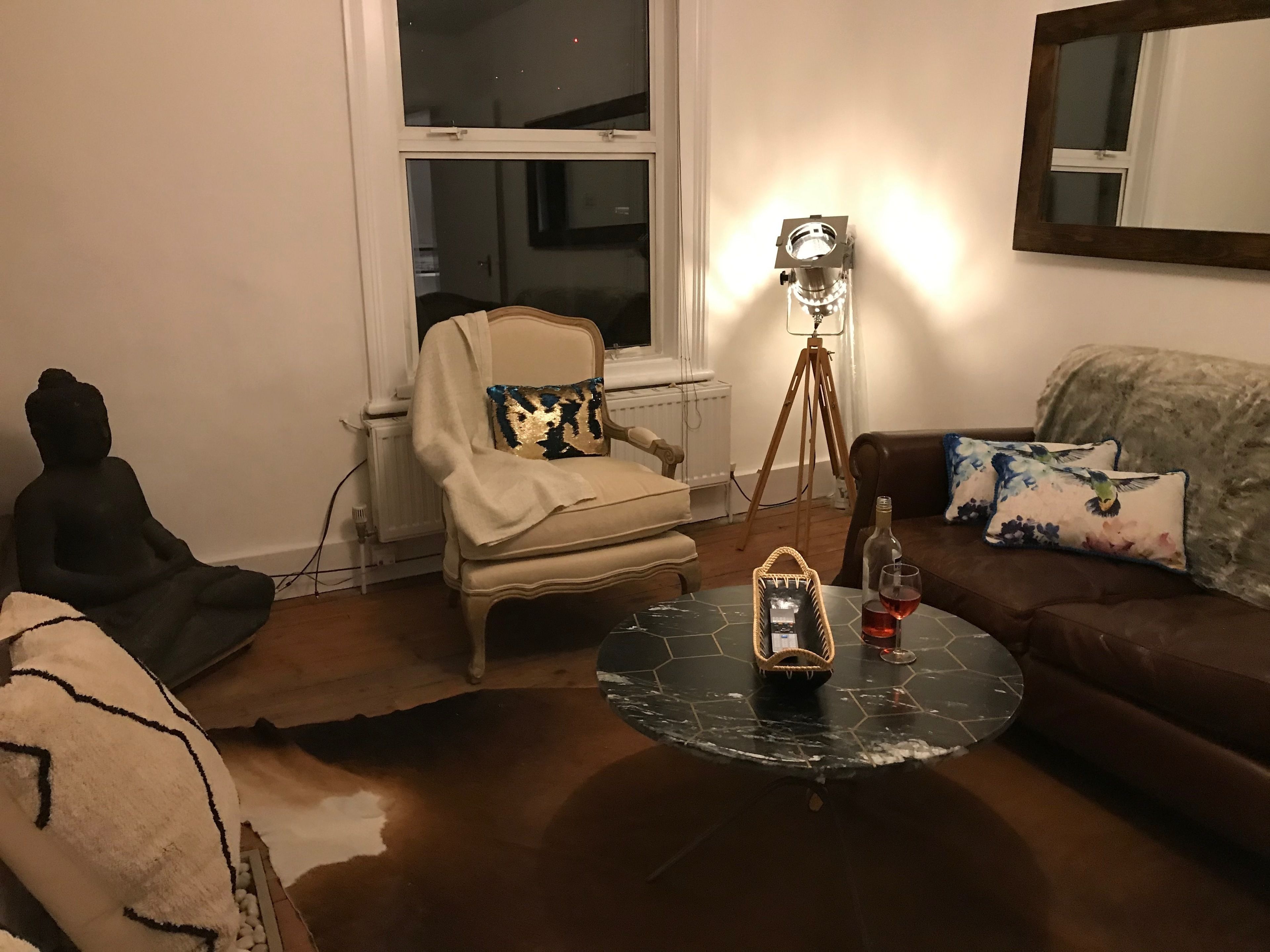 A living room with a meditation chair, a floor lamp, a coffee table with a basket and wine glass, and a sofa with floral cushions.