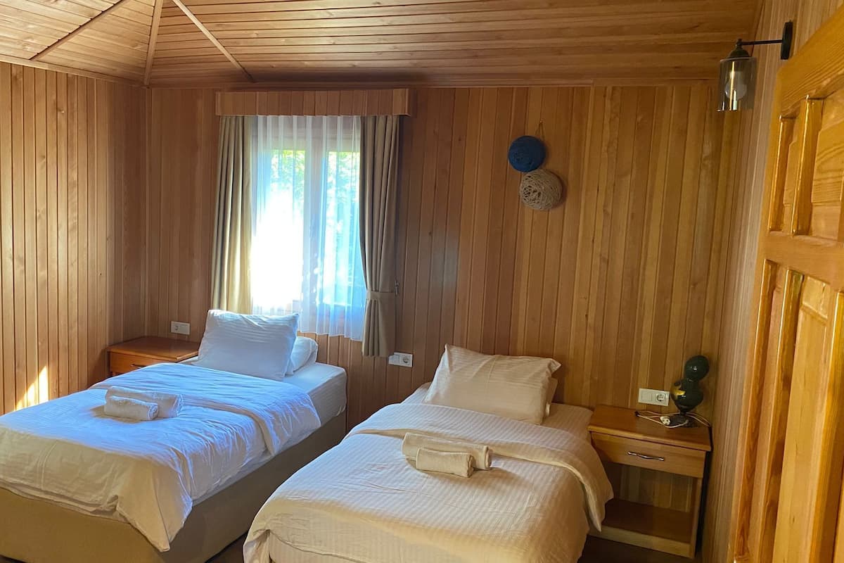 Une chambre avec deux lits, des murs en bois, une fenêtre avec des rideaux et une petite table avec une lampe.
