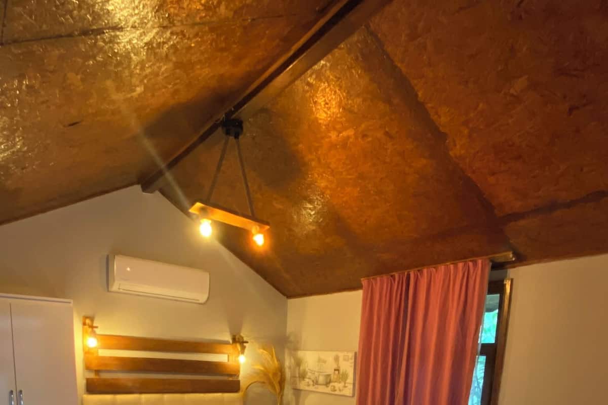 Une chambre avec deux lits, un plafond en bois, un climatiseur blanc et une fenêtre avec des rideaux.