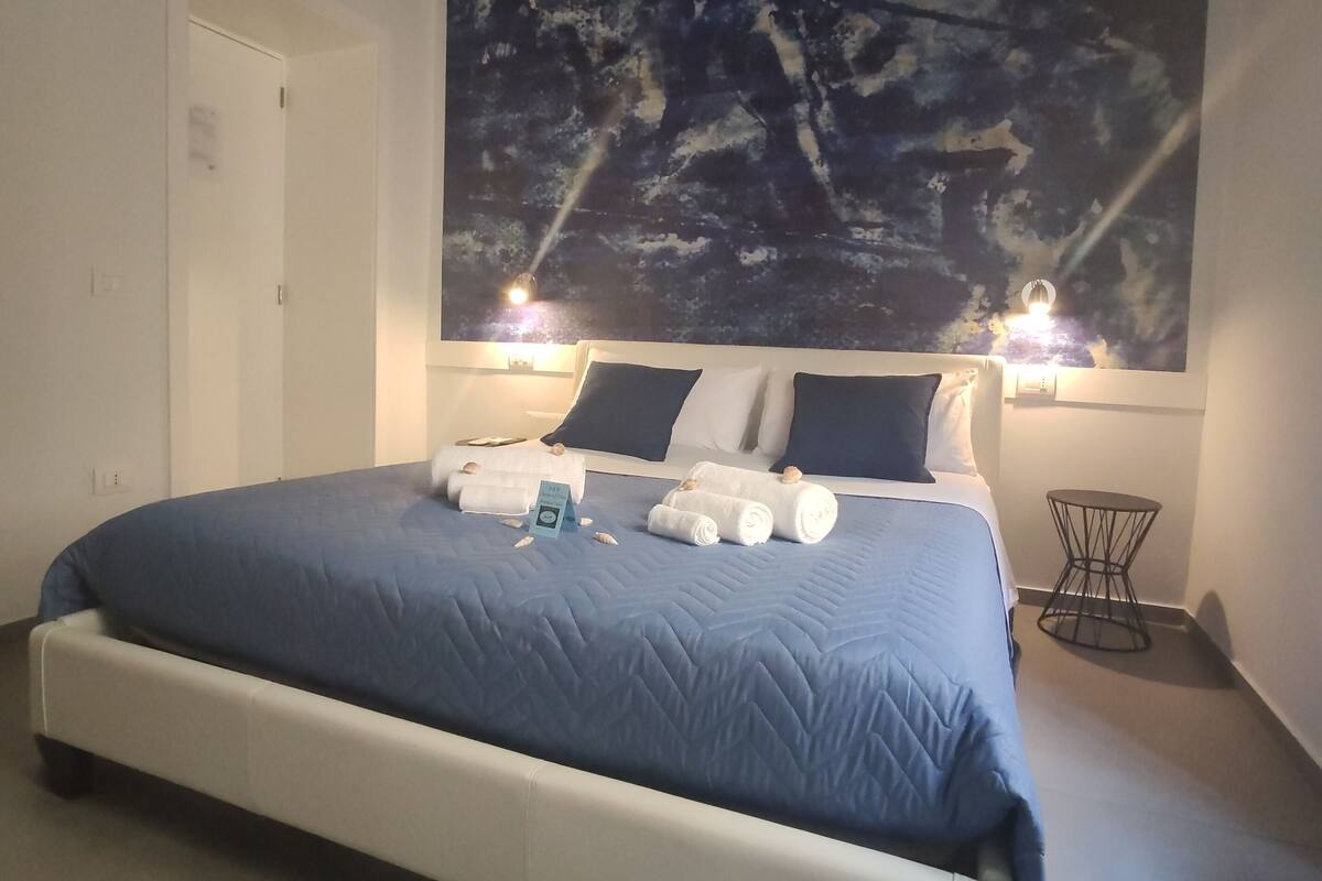 A modern bedroom with a large bed, a ceiling mural, and a small side table.