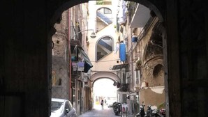 A narrow cobblestone street with an archway leading to a building with balconies and a staircase. - L'arco e il vico (Naples)