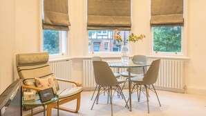 A cozy room with a dining table, chairs, a radiator, and large windows with blinds.