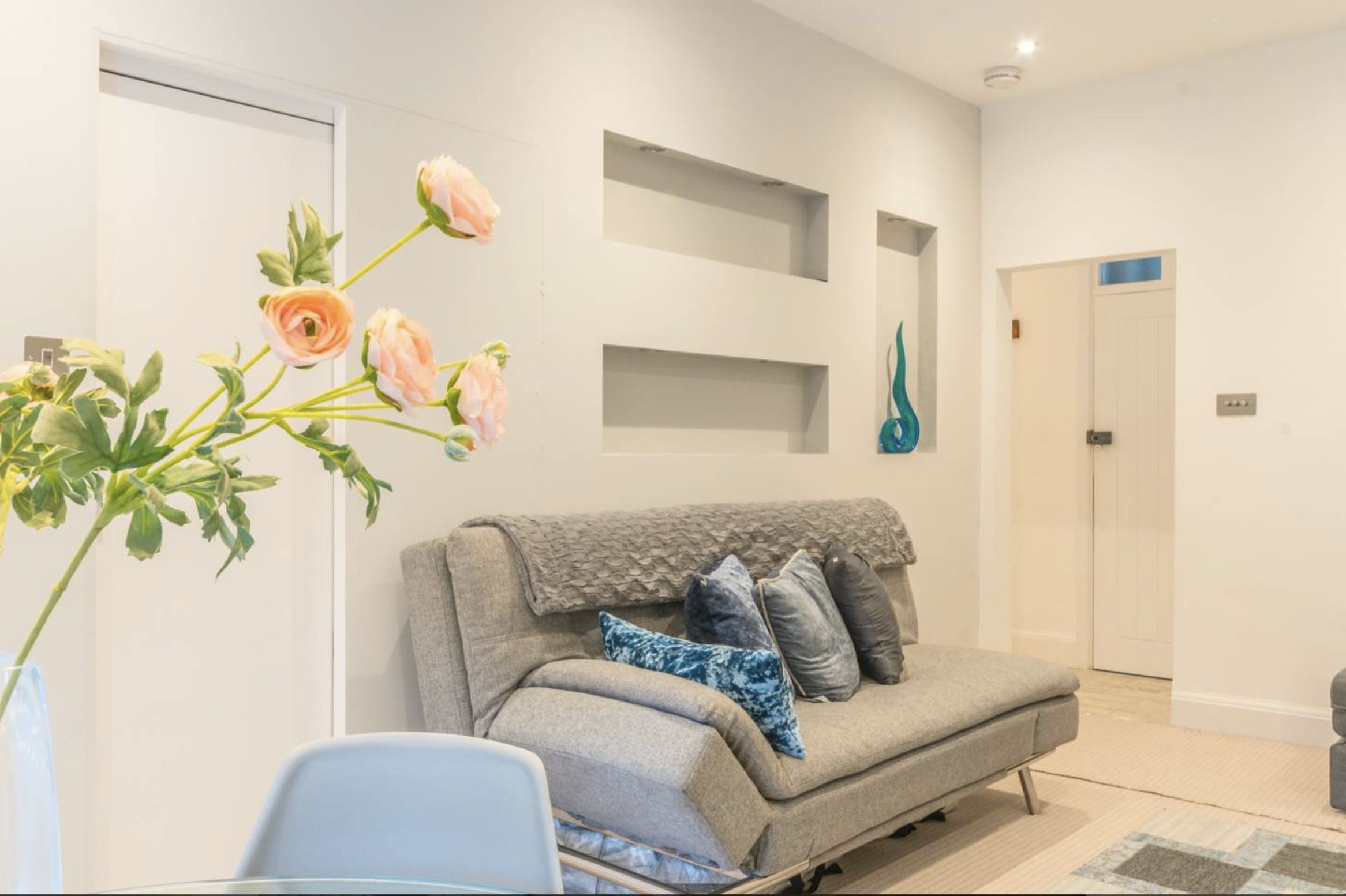 A modern living room with a grey sofa, a glass coffee table, and a vase with flowers.