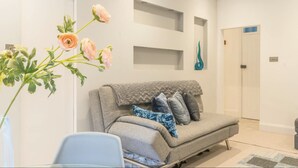 A modern living room with a grey sofa, a glass coffee table, and a vase with flowers.