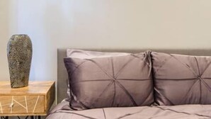 A bedroom with a bed, a framed picture on the wall, a nightstand, and a decorative vase.