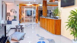 A modern hotel lobby with a reception desk, seating area, and a large TV screen. - Piccadilly Suites and Rooms (Nardò)