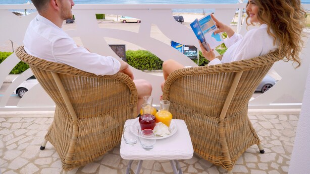 Two people seated at a table with a view of the ocean, a wicker chair, a white table, and a plate with drinks. - Piccadilly Suites and Rooms (Nardò)