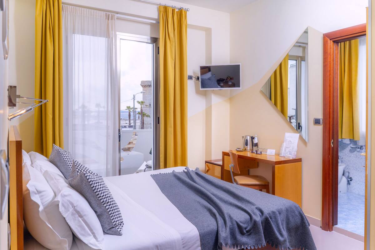 A hotel room with a bed, a desk, a chair, a TV, and a bathroom visible through an open door.
