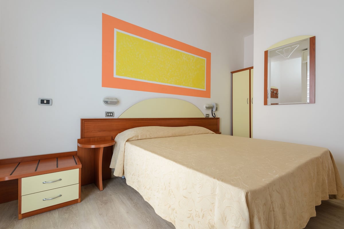 A bedroom with a bed, bedside table, and a small desk with drawers.