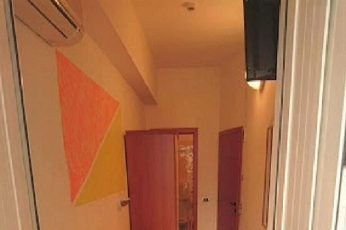 A narrow hallway leading to a bedroom with a bed, a wardrobe, and a door.