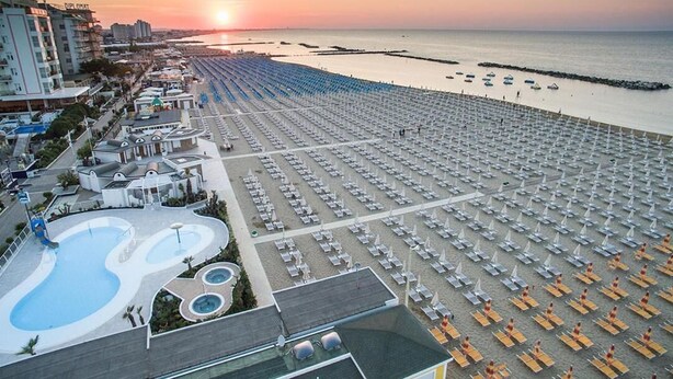 Ein Strandresort mit großem Poolbereich, zahlreichen Liegestühlen und Blick auf den Sonnenuntergang über dem Meer.