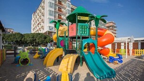 Ein Kinderspielplatz mit Rutschen und Klettergerüsten, umgeben von Gebäuden und einem klaren Himmel.