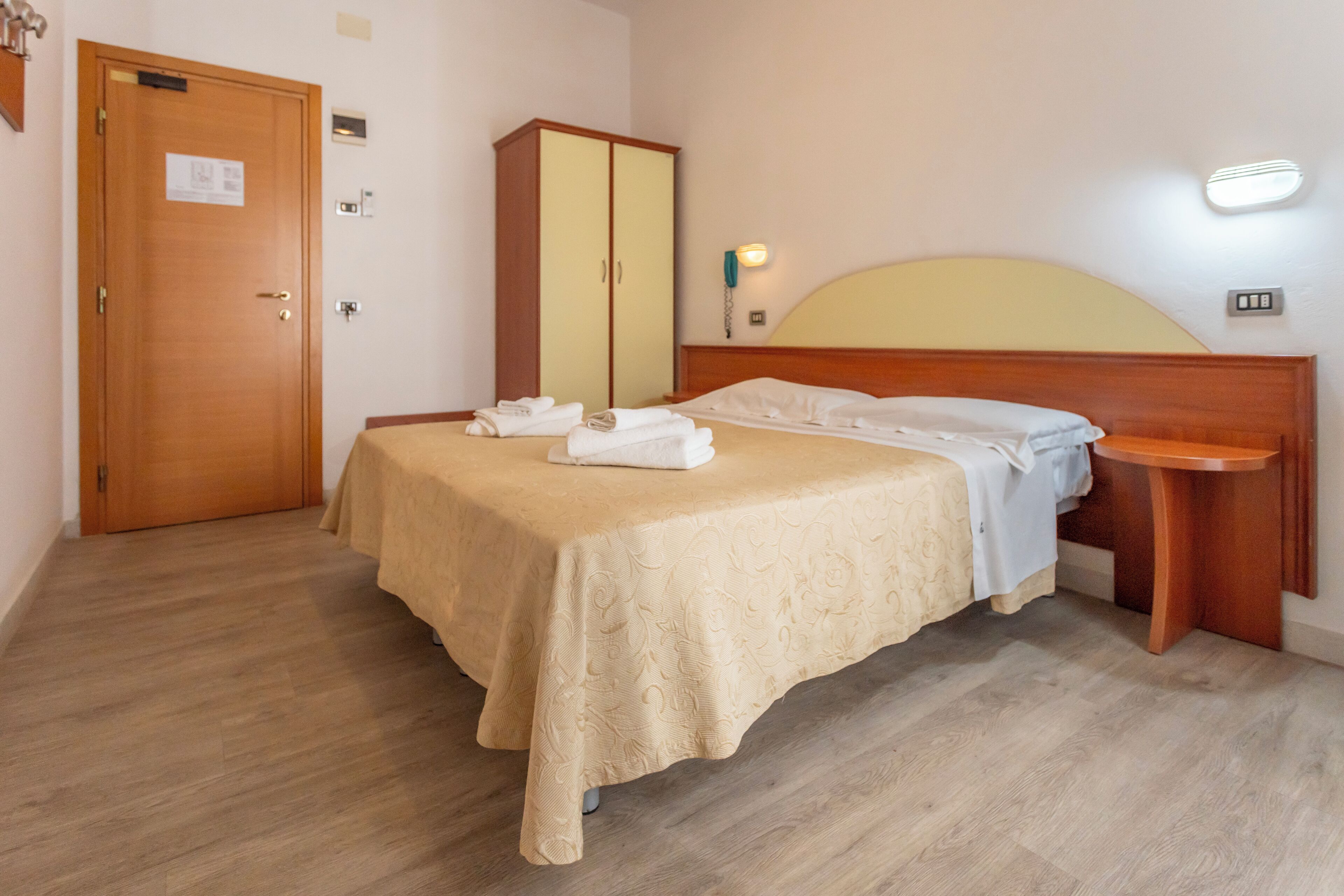 Una camera d'albergo con un letto, un armadio, un comodino e un telefono a muro.
