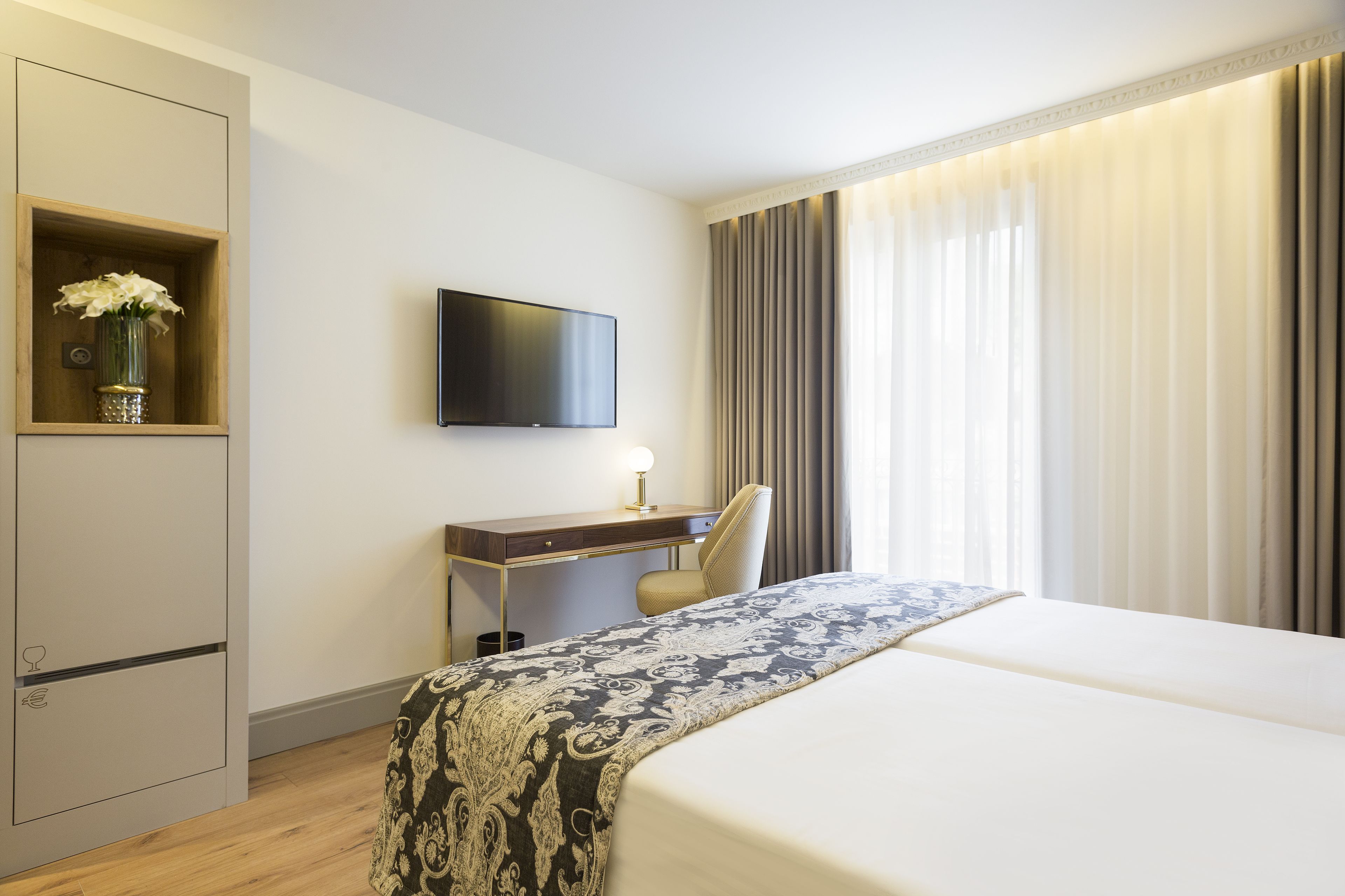 Een hotelkamer met een bed, een bureau met stoel, een televisie en een raam met gordijnen.