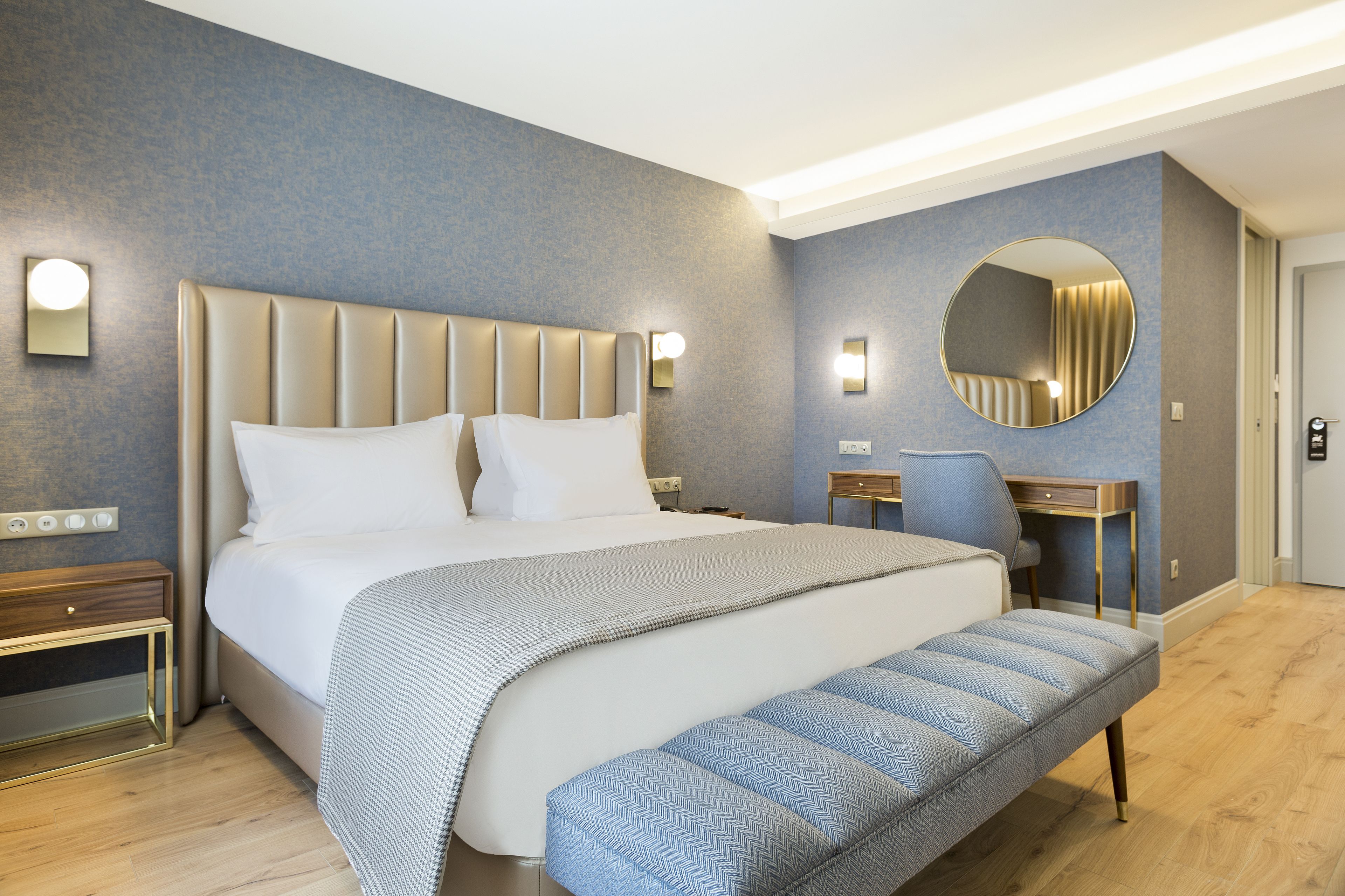 Una habitación de hotel moderna con una cama grande, mesitas de noche, un escritorio y un espejo.