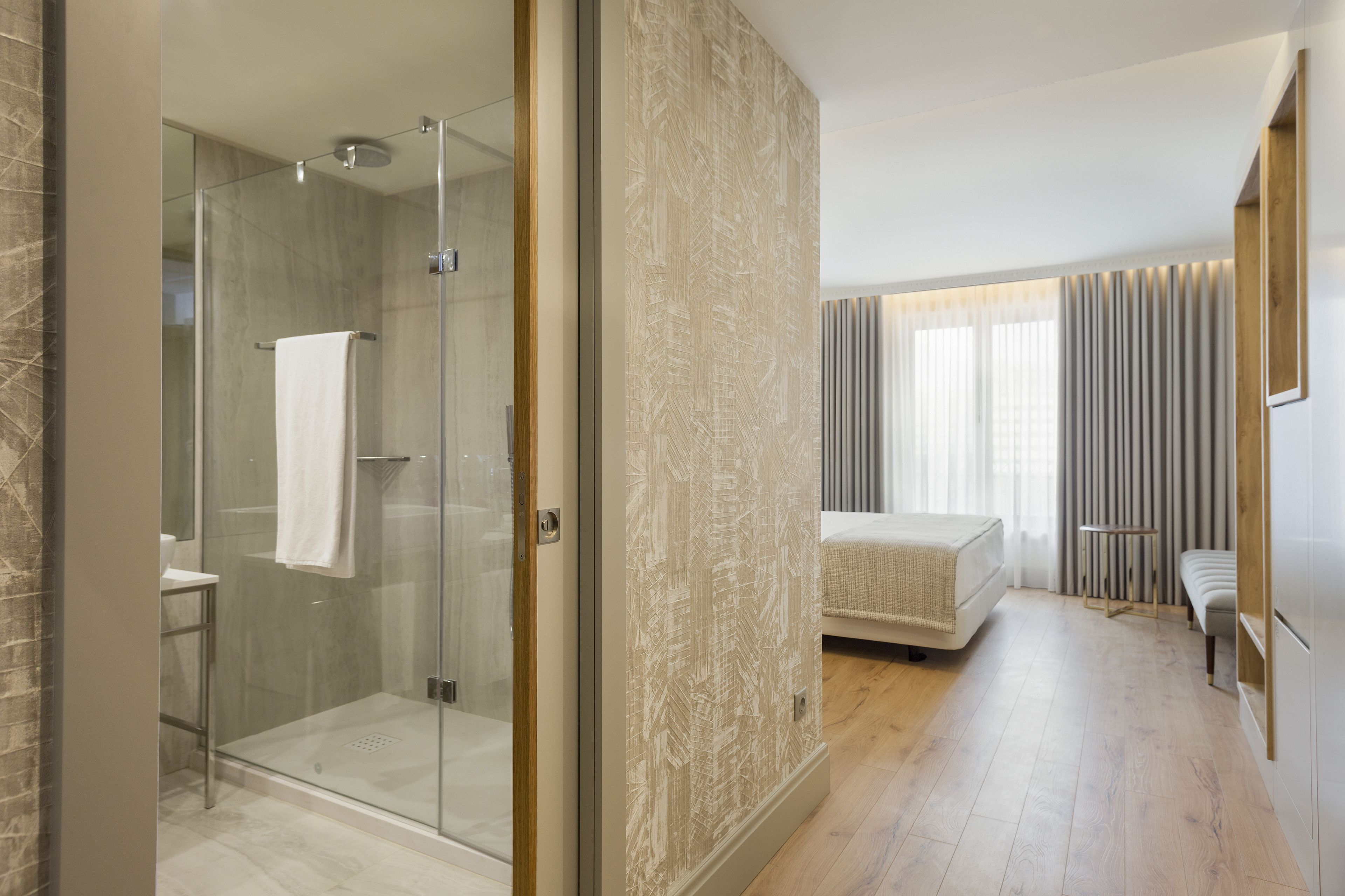 A modern hotel room with a glass-enclosed shower, a bed, and a bedside table.