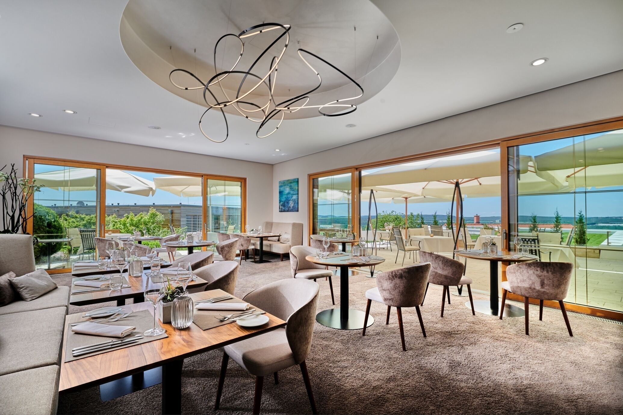 A modern dining area with large windows, a central chandelier, and a view of the outdoors.