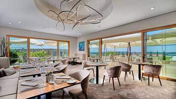 A modern dining area with large windows, a central chandelier, and a view of the outdoors.