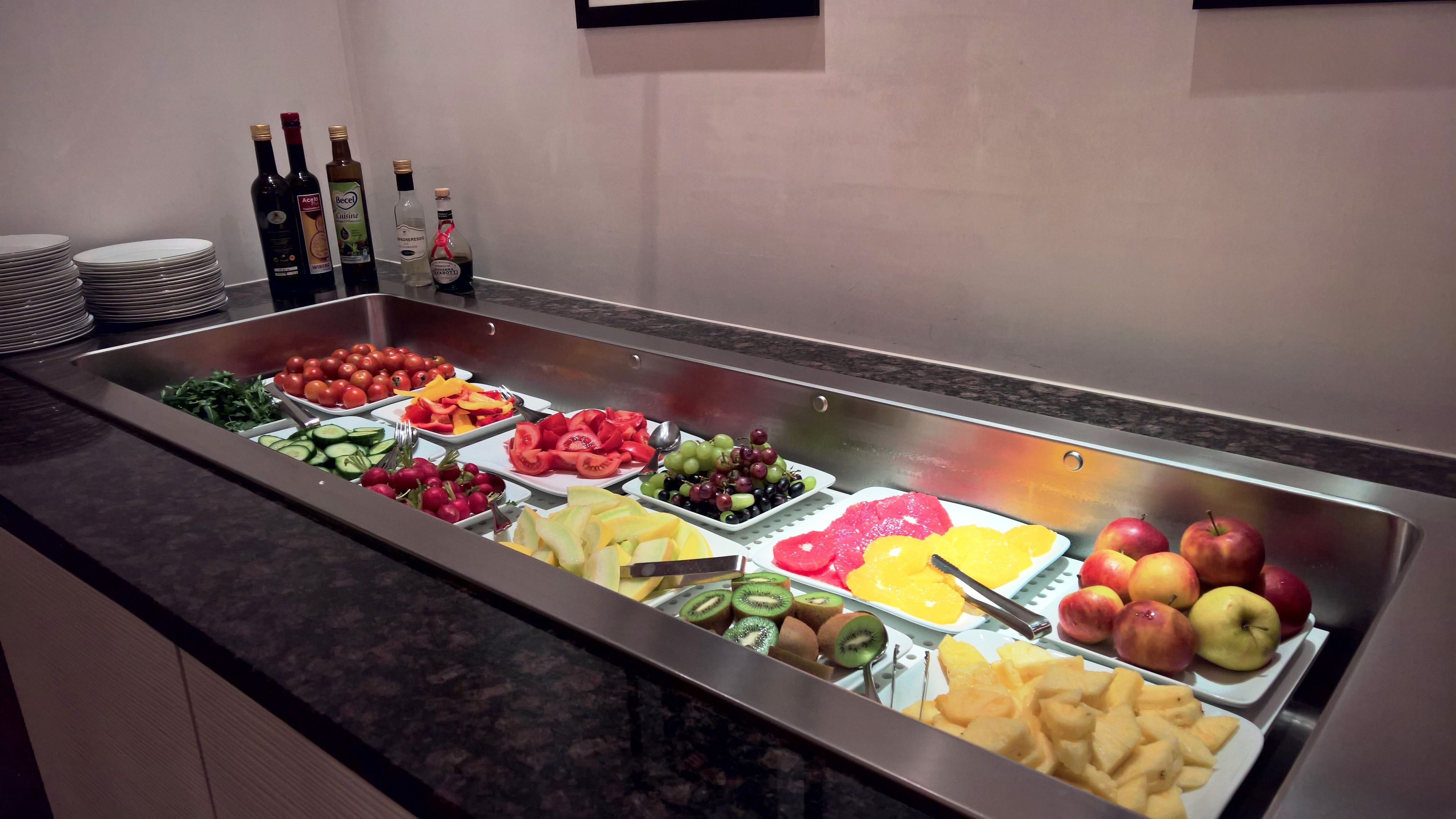 A buffet with various fruits and vegetables, including tomatoes, cucumbers, and apples.