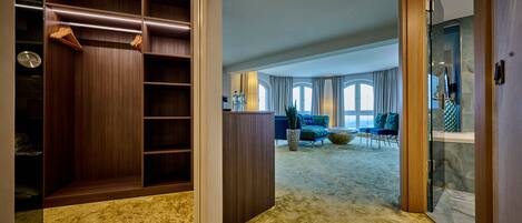 Amplia habitación con un vestidor grande, una zona de estar con un sofá y sillones azules, y vistas al exterior a través de amplios ventanales.