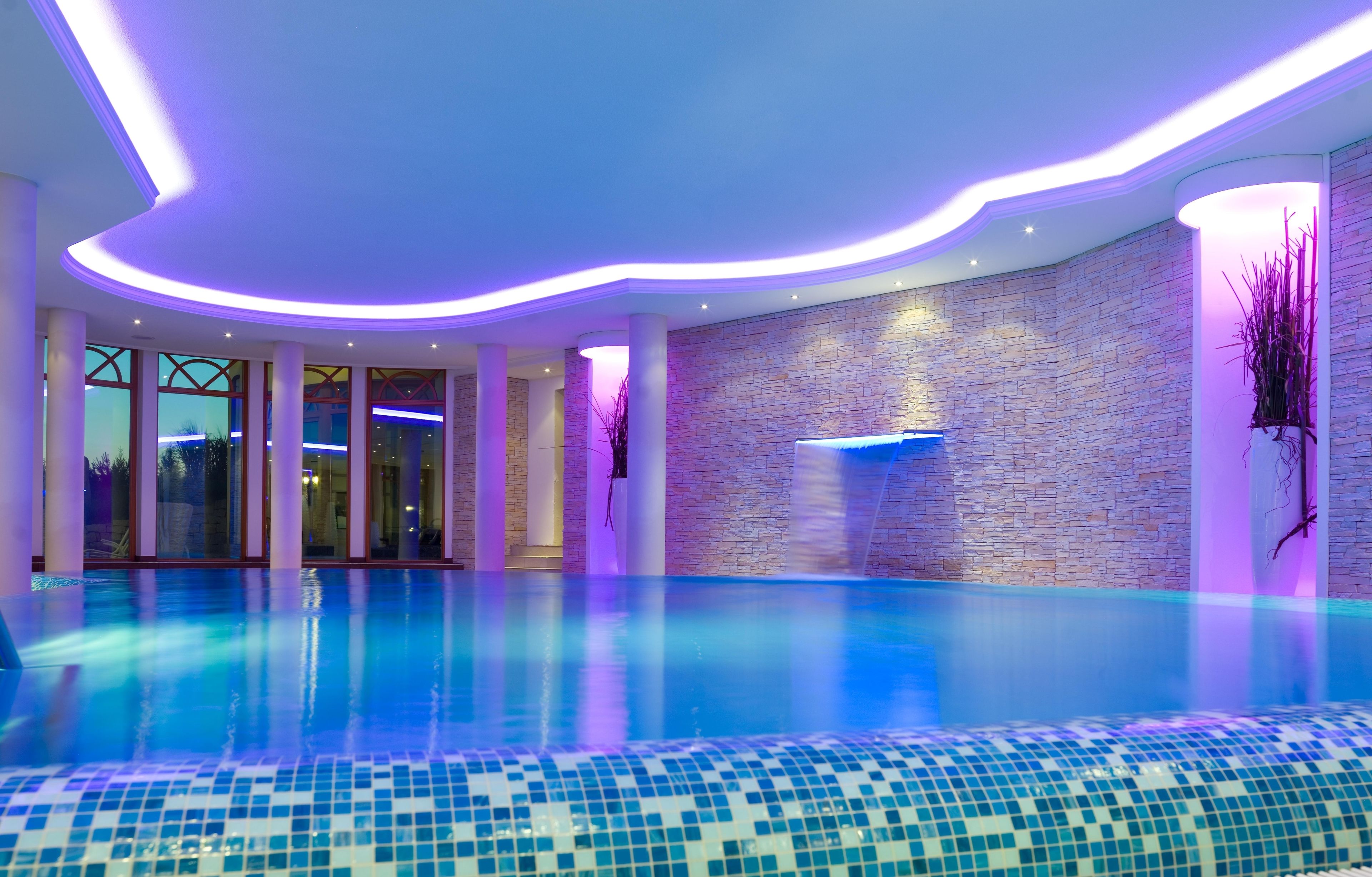 A modern indoor swimming pool with a stone wall and glass doors leading to an outdoor area.