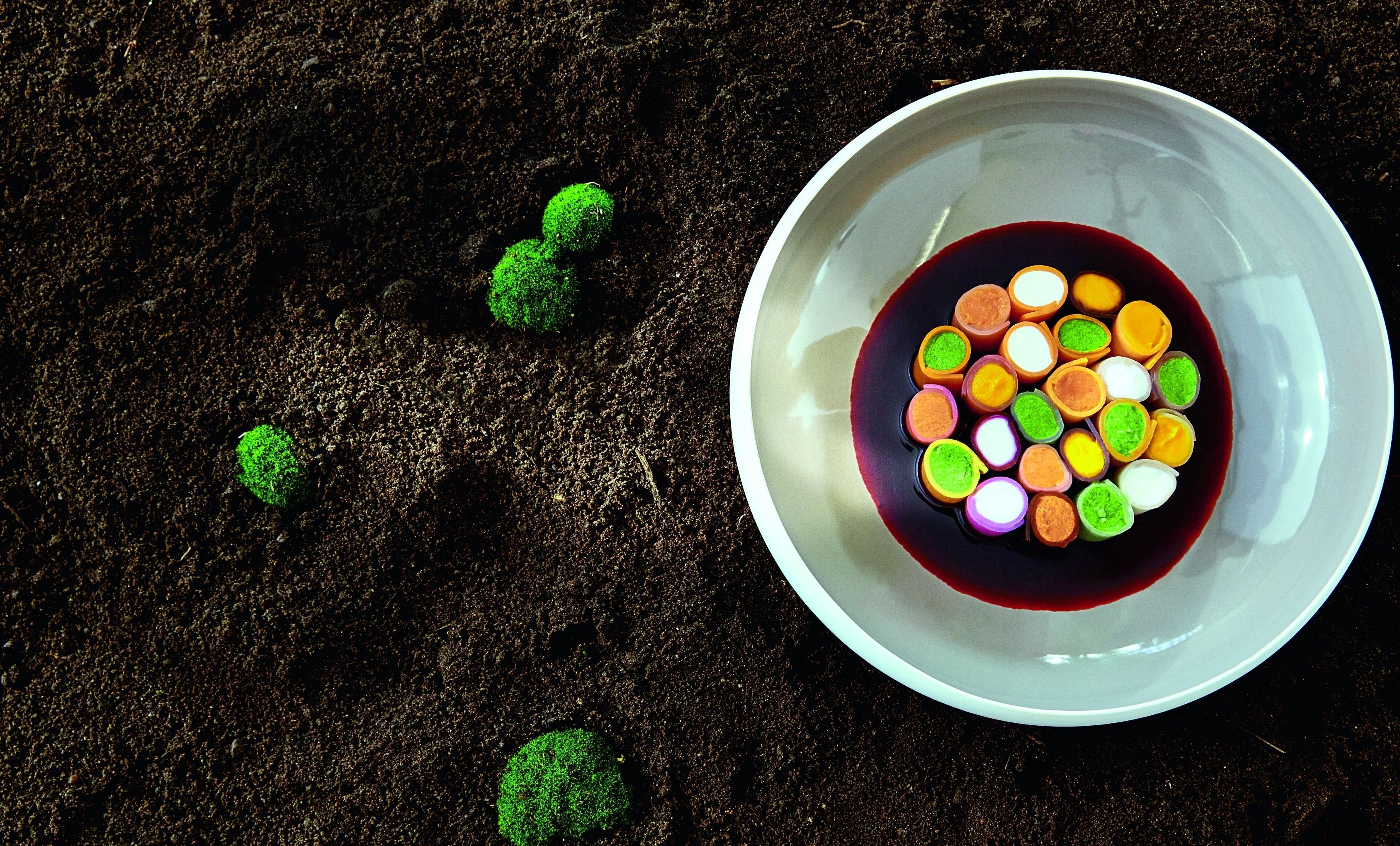 Une assiette blanche avec des bonbons colorés et un liquide foncé sur une surface sombre.