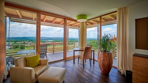 Een ruim balkon met een houten vloer, een beige bank, een eettafel en een grote potplant.